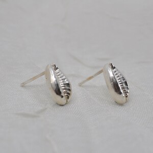May include: A pair of silver earrings shaped like seashells. The earrings have a textured surface and are designed to be worn as studs.