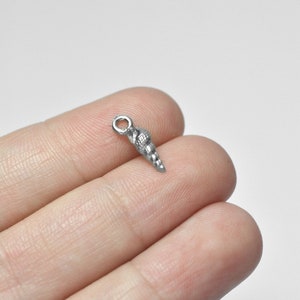 Puede incluir: Un amuleto de concha de mar plateado con un bucle para sujetarlo a joyas u otras manualidades.