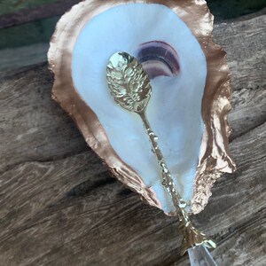May include: A gold-rimmed oyster shell dish with a gold spoon with a crystal tip. The spoon has a floral design.