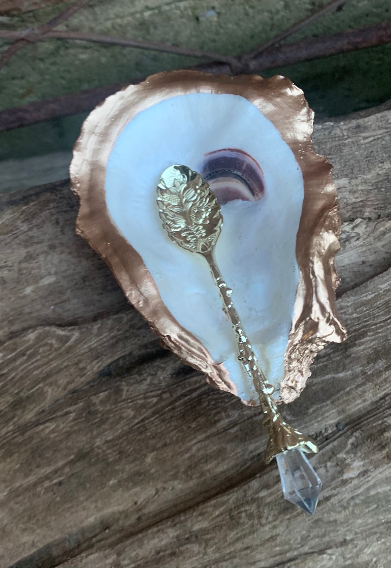May include: A gold-rimmed oyster shell dish with a gold spoon with a crystal tip. The spoon has a floral design.