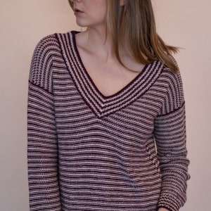May include: A burgundy and cream striped V-neck sweater. The long-sleeved sweater has a ribbed hem and cuffs. The neckline and shoulder seams are also ribbed. The sweater is made of a soft, knitted material.