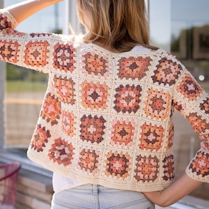 May include: A crocheted cardigan with a granny square pattern in shades of brown, pink, and white.