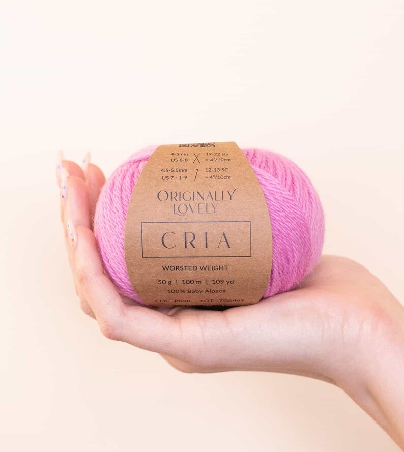 May include: A ball of pink worsted weight yarn labeled "Originally Lovely CriA" with the details: 50 g | 100 m | 109 yd, 100% Baby Alpaca, and needle size recommendations.