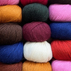 May include: A collection of 10 balls of yarn in various colors, including pink, red, green, brown, burgundy, white, blue, orange, and dark brown. The yarn is arranged in three rows of balls.