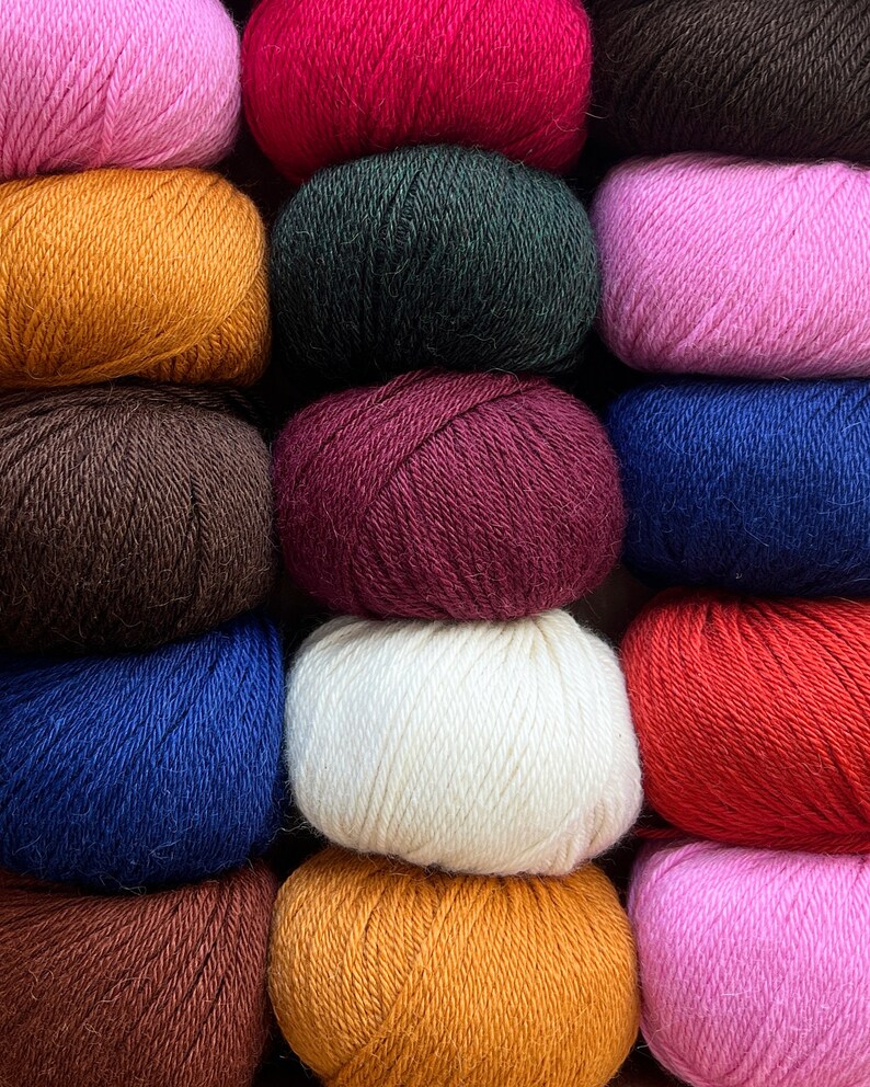 May include: A collection of 10 balls of yarn in various colors, including pink, red, green, brown, burgundy, white, blue, orange, and dark brown. The yarn is arranged in three rows of balls.
