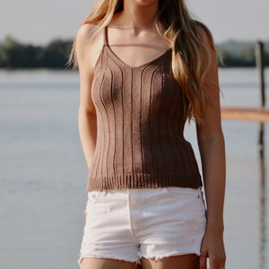 May include: A brown ribbed knit tank top with a v-neckline. The tank top is worn with white denim shorts.