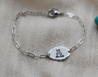 Op de afbeelding: Een zilverkleurige kettingarmband met een ovale bedel met een gehamerde rand. De bedel is gestempeld met de letter A in een decoratief zwart lettertype. De armband heeft een karabijnsluiting en een korte verlengketting.