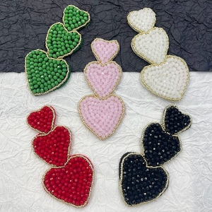 Puede incluir: Tres juegos de adornos de cuentas en forma de corazón en verde, rosa, rojo y negro. Cada juego presenta tres corazones de tamaño decreciente, con un contorno dorado.