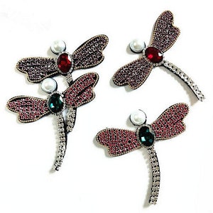 May include: Four decorative dragonfly embellishments with red, green, and white rhinestones. The dragonflies are made of fabric and have a beaded design.