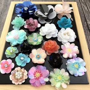 Puede incluir: Surtido de adornos con forma de flor, coloridos, iridiscentes y brillantes. Los adornos están hechos de lentejuelas y cuentas y vienen en una variedad de colores, incluyendo azul, verde, rosa, morado y blanco.