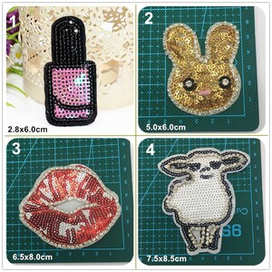 May include: Four iron-on patches with different designs. The first patch is a pink and black nail polish bottle, measuring 2.8 x 6.0 cm. The second patch is a gold bunny rabbit, measuring 5.0 x 6.0 cm. The third patch is a red and white pair of lips, measuring 6.5 x 8.0 cm. The fourth patch is a white sheep, measuring 7.5 x 8.5 cm.
