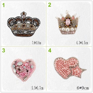 May include: Four embroidered iron-on patches with pearl and rhinestone embellishments. The patches include a crown, a crown with a pink stone, a heart, and a heart with a bow. The patches are approximately 7.8 inches by 10.8 inches, 4.3 inches by 4.5 inches, 5.5 inches by 5.7 inches, and 6 inches by 9 inches.