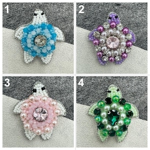 May include: Four beaded turtle brooches in different colors. The turtles are made with white beads and have a large crystal in the center. The turtles are surrounded by smaller beads in different colors, including blue, pink, purple, and green.