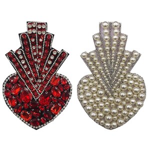 Peut inclure: Deux patchs brodés en forme de cœur, l'un avec des strass rouges et transparents et l'autre avec des perles blanches.
