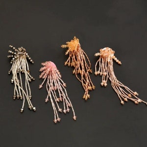 Könnte beinhalten: Vier Paar geperlte Ohrhänger in Silber, Rosa, Gold und Roségold. Die Ohrringe bestehen aus kleinen Perlen, die zu einem langen, fließenden Design zusammengefügt sind.