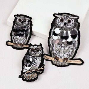 May include: Three embroidered owl patches featuring silver sequins. The owls are perched on branches with brown and gold accents.