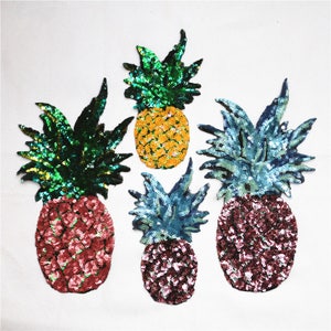 May include: Four pineapple-shaped sequined patches in different colors. The patches are green, blue, yellow, and pink. They are all about 4 inches tall.
