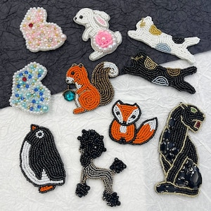 Puede incluir: Surtido de apliques de animales con cuentas, que incluyen un conejo, un gato, una ardilla, un zorro, un pingüino, un caniche y una pantera. Los apliques están hechos con cuentas y lentejuelas de colores.