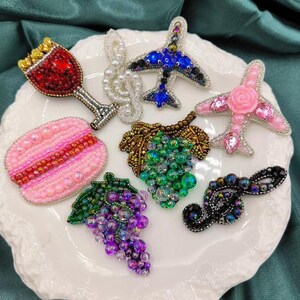 May include: Assortment of colourful beaded iron-on patches, including a wine glass, a plane, a flower, a grape bunch, a musical note, and a macaron.