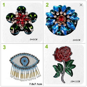 Puede incluir: Cuatro parches termoadhesivos con diferentes diseños. El primer parche es una flor verde con pedrería roja y blanca. El segundo parche es una flor azul con pedrería roja y blanca. El tercer parche es un ojo blanco con cuentas azules y doradas. El cuarto parche es una rosa roja con hojas verdes. Los parches miden 5x5 cm y 7,8x7,1 cm.