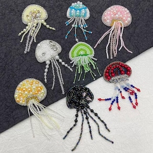 May include: Assortment of ten beaded jellyfish appliques in various colours, including white, pink, blue, green, black, and red. Each applique features a beaded body and dangling beaded tentacles.