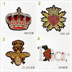 May include: Four embroidered iron-on patches with various designs. The first patch is a gold crown with red jewels, measuring 8 by 7 centimeters. The second patch is a gold heart with red jewels and a crown, measuring 10 by 9.5 centimeters. The third patch is a gold bee with a crown, measuring 13.5 by 13 centimeters. The fourth patch is a white "Dior" with red flowers and pearls, measuring 18 by 9 centimeters.