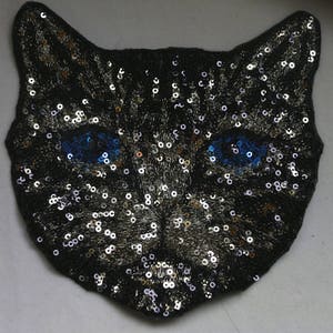 May include: A black cat face patch with silver and gold sequins and blue eyes. The patch is made of fabric and is perfect for adding a touch of whimsy to clothing or accessories.