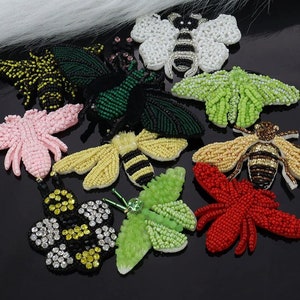 以下が含まれることがあります： 蜂、蝶、蛾など、さまざまな昆虫のデザインが施された刺繍のアイロン接着パッチの詰め合わせ。パッチはカラフルなビーズとスパンコールでできています。