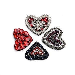 May include: Four heart-shaped patches with red, black and white rhinestone embellishments. The patches are made of fabric and have a felt backing.