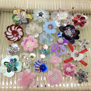 Puede incluir: Surtido de flores decorativas de colores, brillantes y con cuentas. Estas piezas decorativas son perfectas para agregar un toque de brillo a la ropa, los bolsos y otras manualidades.