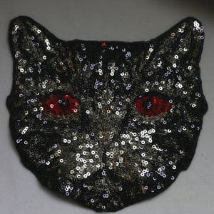 May include: Black cat face applique with gold and silver sequins and red eyes.
