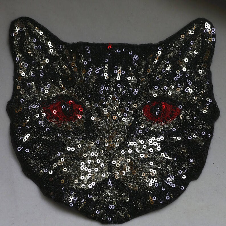 May include: Black cat face applique with gold and silver sequins and red eyes.