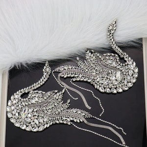 May include: Two silver swan-shaped embellishments with crystal rhinestones and dangling chains.
