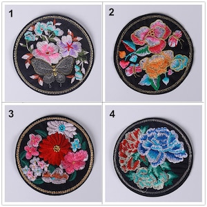 May include: Four embroidered patches with floral designs. Each patch is circular and features a different arrangement of flowers and butterflies. The patches are on a black background with gold trim.