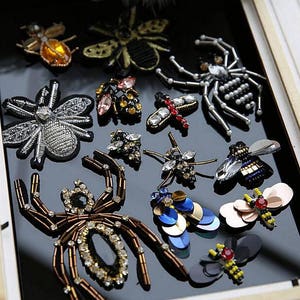 May include: Assortment of colorful beaded insect and spider appliques. The appliques feature various designs, including butterflies, dragonflies, bees, and spiders. The appliques are made with beads, sequins, and other embellishments.