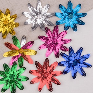 May include: Assortment of eight colorful sequin flower embellishments. The flowers are in shades of gold, silver, pink, blue, green, and red. Each flower has a starburst shape with a center bead.