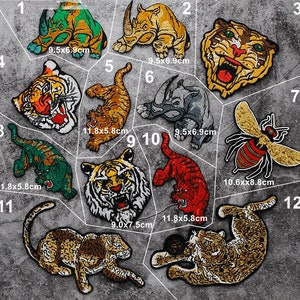 Puede incluir: Doce parches termoadhesivos con diferentes diseños de animales, incluyendo tigres, rinocerontes, una abeja y un leopardo. Los parches son de diferentes tamaños y colores, y algunos tienen texto. Los parches están sobre un fondo gris.