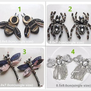 May include: Four sets of iron-on patches featuring different designs. The first set is two gold and black bees, the second set is two black and silver spiders, the third set is two pink and blue dragonflies, and the fourth set is two silver and white beaded tassels. The patches are all approximately 6-8 cm in size.