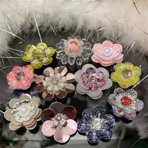Puede incluir: Surtido de adornos con forma de flor de colores con lentejuelas, cuentas y pedrería. Estas piezas decorativas son perfectas para añadir un toque de brillo a la ropa, los accesorios y las manualidades.