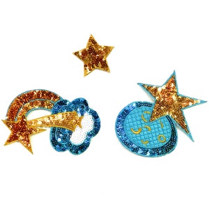 May include: Three gold and blue sparkly iron-on patches. One patch is a shooting star with a cloud, another is a star, and the last is a circle with a star on top.