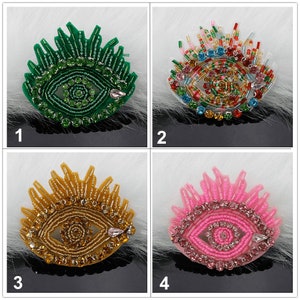 以下が含まれることがあります： 異なる色のビーズとラインストーンで刺繍された4つのアイパッチ。アイパッチは緑、赤、金、ピンクです。