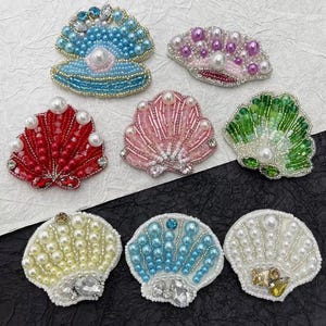 Puede incluir: Surtido de diez adornos de conchas de mar con cuentas de colores. Los adornos están hechos de cuentas y lentejuelas de varios colores, incluyendo azul, verde, rojo, rosa y blanco. Los adornos tienen forma de conchas marinas y tienen un centro nacarado.