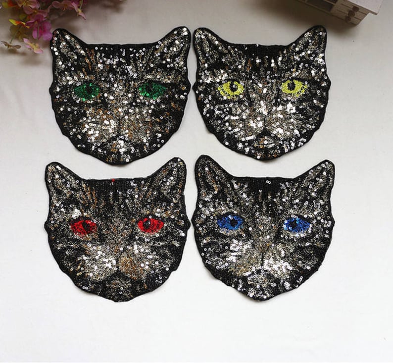 May include: Four black cat-shaped iron-on patches with colorful sequin details. The cats have different colored eyes: green, yellow, red, and blue.