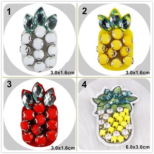 Puede incluir: Cuatro adornos de cuentas con forma de piña. El primero es blanco, el segundo es amarillo, el tercero es rojo y el cuarto es verde y amarillo con pedrería. Cada uno mide 3 cm por 1,6 cm excepto el cuarto, que mide 6 cm por 3 cm.