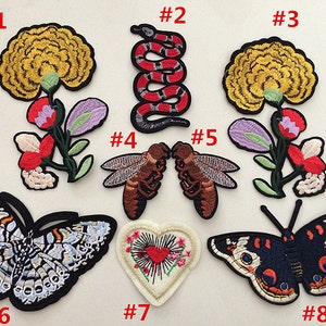 Könnte beinhalten: Acht Bügelbilder mit verschiedenen Designs, darunter Blumen, Schmetterlinge, Schlangen und Bienen. Die Patches sind farbenfroh und detailliert, mit einer Vielzahl von Texturen und Mustern.