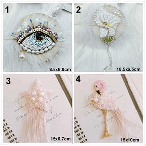 May include: Four embroidered patches with different designs. The first patch is a blue eye with gold and iridescent sequins. The second patch is a white flower with green leaves. The third patch is a pink star with white pearls. The fourth patch is a pink flamingo with gold accents. The patches are all on a white background.
