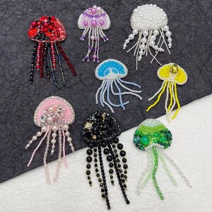 May include: Assortment of colourful beaded jellyfish appliques. Each applique features a different colour scheme and bead design. The jellyfish are made with various beads, including pearls, sequins, and glass beads.