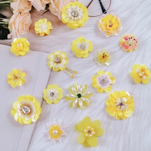 May include: Assortment of yellow, white, and pink fabric flower embellishments with pearl and rhinestone accents.