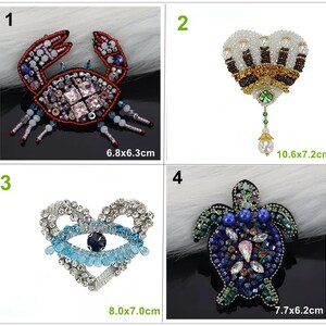 May include: A collection of four beaded brooches: a red crab measuring 6.8x6.3cm, a heart-shaped crown with a pearl drop measuring 10.6x7.2cm, a heart-shaped eye motif measuring 8.0x7.0cm, and a blue and green sea turtle measuring 7.7x6.2cm.