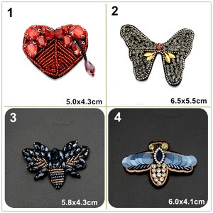 May include: Four embroidered iron-on patches with different designs. The first patch is a red heart with red and clear rhinestones. The second patch is a gray butterfly with gold accents and clear rhinestones. The third patch is a black and blue bee with clear rhinestones. The fourth patch is a blue and green bee with clear rhinestones. The patches are approximately 5 cm in size.